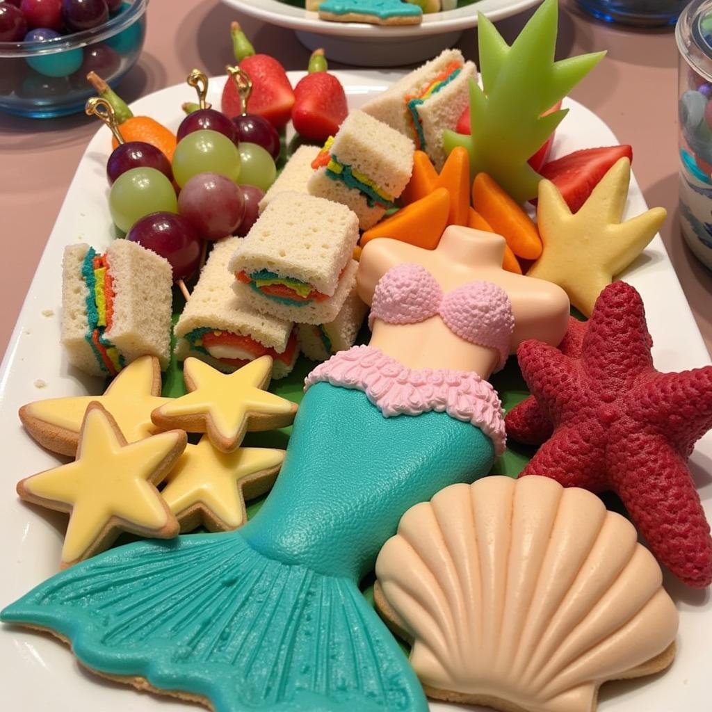 A platter of colorful mermaid-themed finger foods including sandwiches, fruit skewers, and cookies.