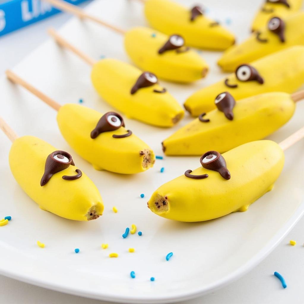 A platter of banana pops dipped in yellow chocolate and decorated with minion eyes.