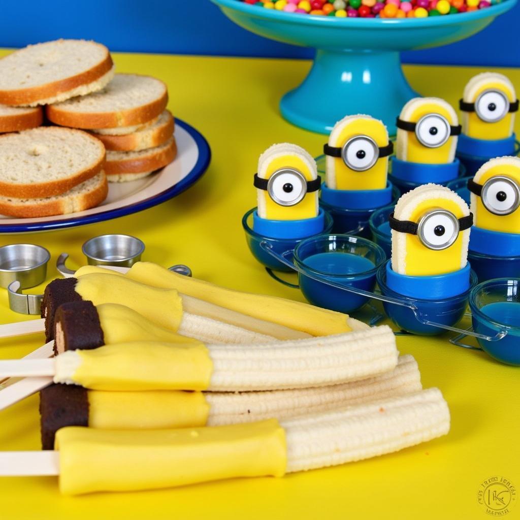 A vibrant spread of minion-themed party food, including banana pops, blue jello cups, and minion-shaped sandwiches.